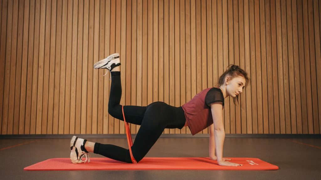 Caucasian woman practicing fitness on a mat with a resistance band in a gym setting.