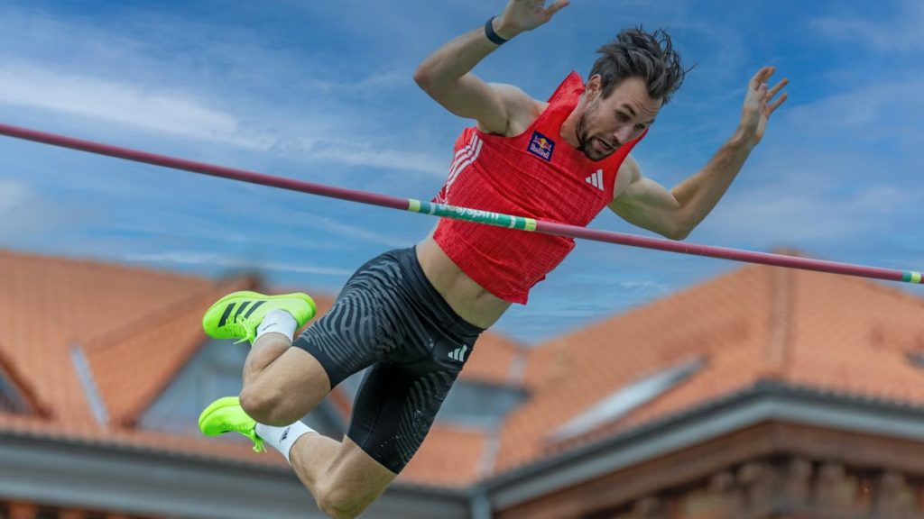 A male athlete captured mid-air during a pole vault attempt against a clear sky.